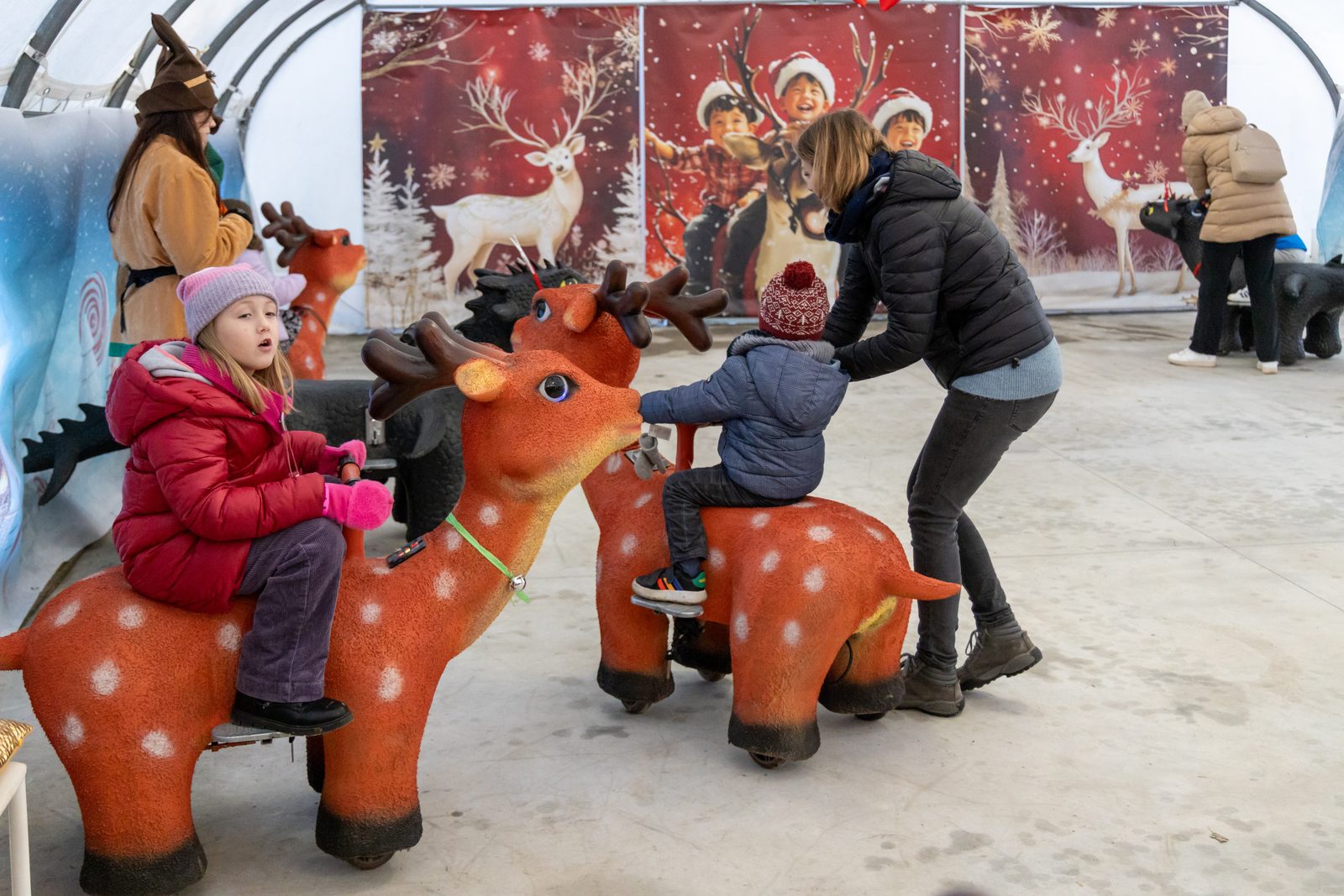 Bambini che giocano sulle renne nell’area coperta del Villaggio degli elfi alla Grotta di Babbo Natale