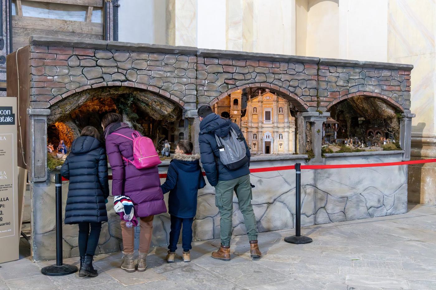 Famiglia che guarda il presepe e l’esposizione artistica alla Chiesa della Guardia durante la Grotta di Babbo Natale