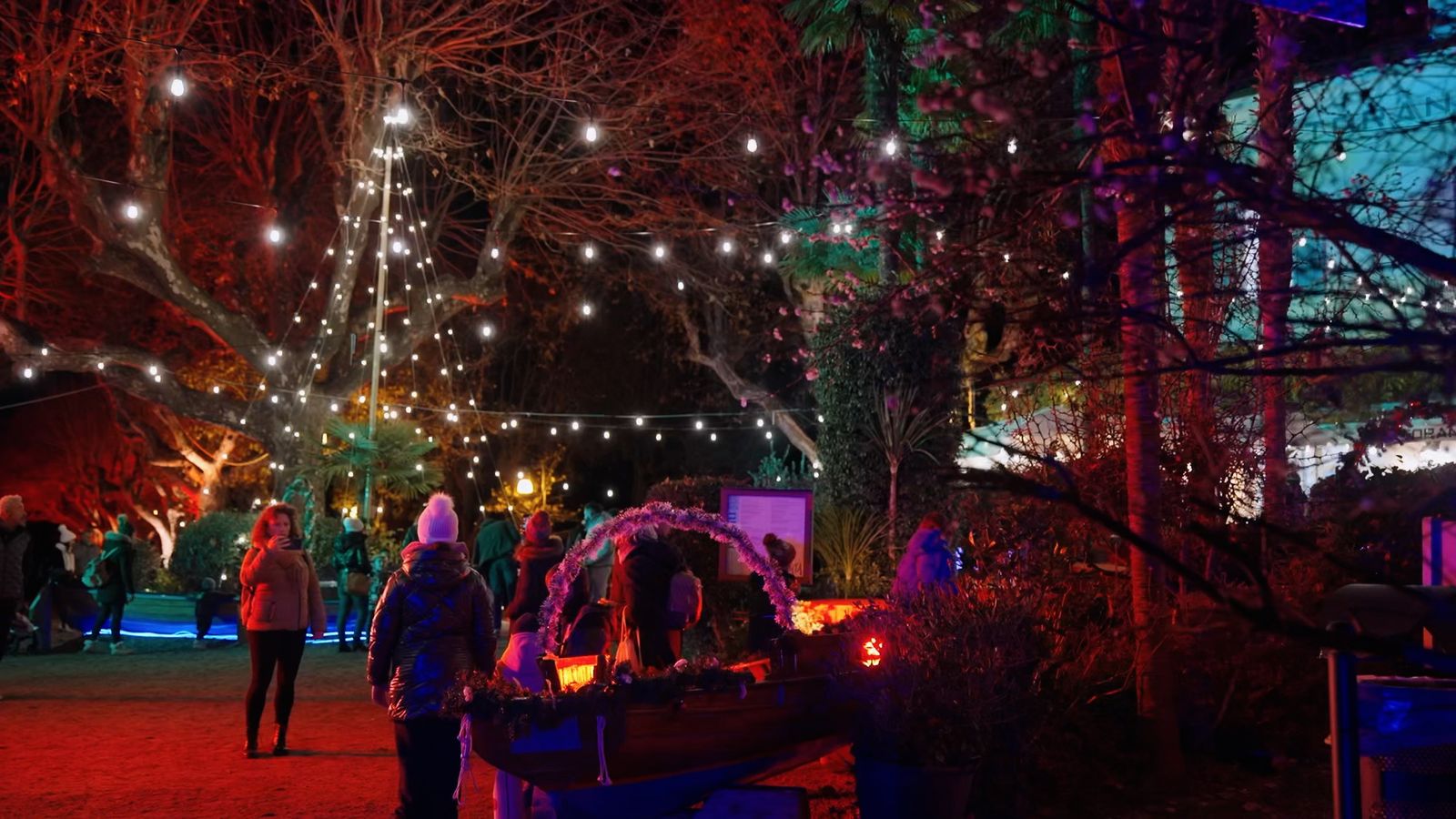 Percorso illuminato con luci a festone, alberi colorati e barca decorata all’interno delle Isole di Luce a Baveno