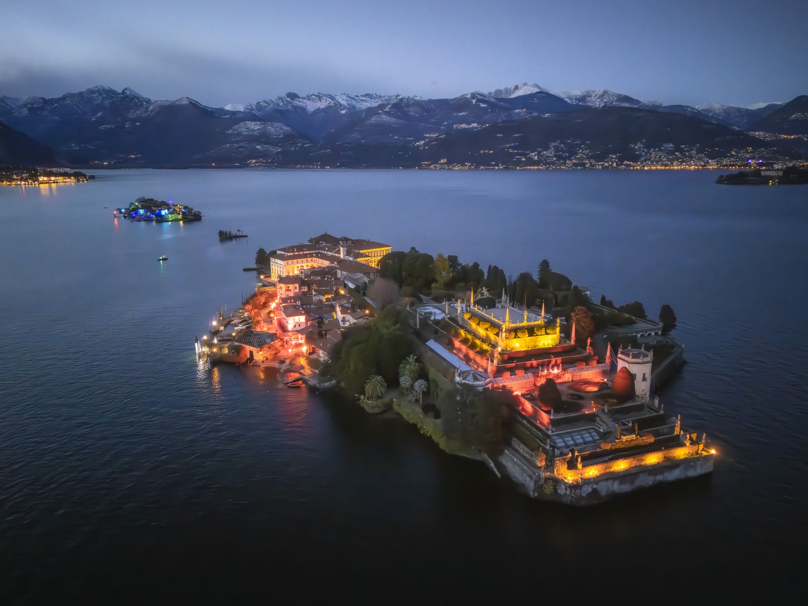 Giardini terrazzati di Isola Bella illuminati d’oro e rosso per le Isole di Luce, con Isola Pescatori e Alpi innevate