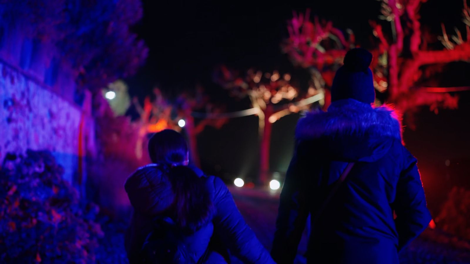 Genitore e bambino in passeggiata notturna tra le luci blu e rosse sull’Isola Pescatori durante le Isole di Luce