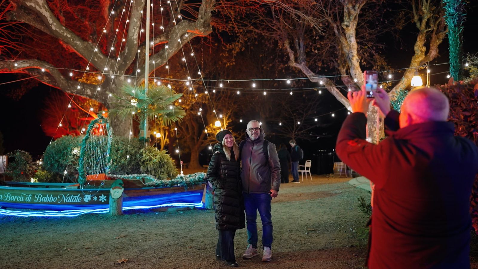 Coppia fotografata davanti alla Barca di Babbo Natale illuminata al Molo delle Luci di Baveno, Isole di Luce