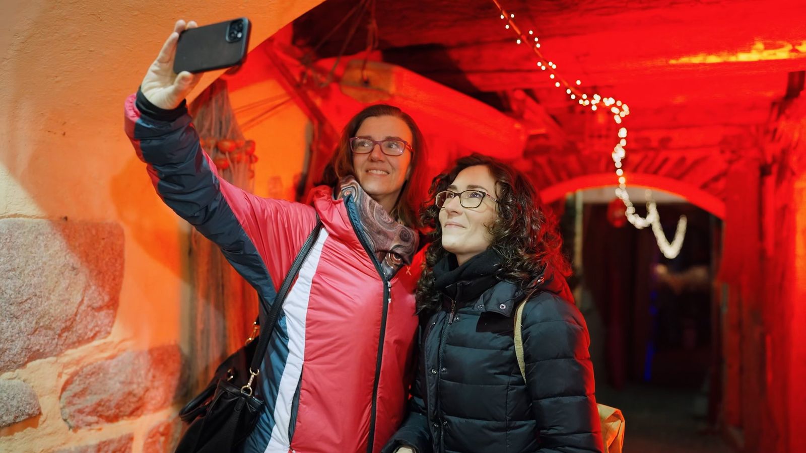 Due visitatrici si scattano un selfie in un vicolo illuminato di rosso sull’Isola Pescatori durante le Isole di Luce
